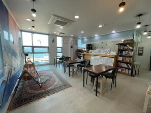 A room with a large window, a bookshelf, and a dining area with tables and chairs.