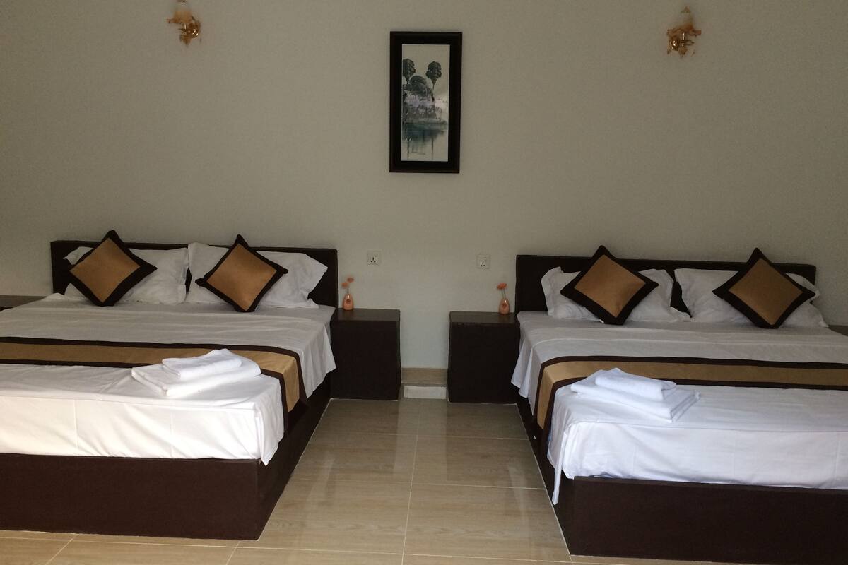 Two identical twin beds with brown headboards and white bedding, a framed picture on the wall, and a tiled floor.