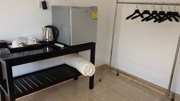 A kitchenette with a refrigerator, coffee maker, and tea kettle on a black countertop. A towel is rolled up and placed on a shelf below.