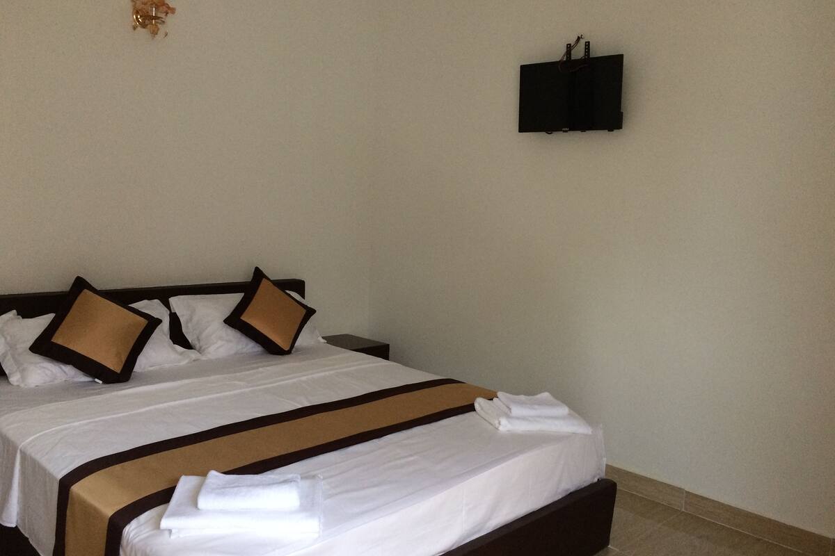A hotel room with a bed, pillows, a flat-screen TV mounted on the wall, and a nightstand.