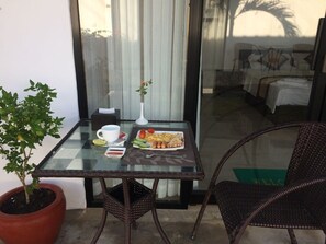 A glass table with a breakfast setting, including eggs, sausages, and vegetables, on a balcony with wicker chairs and a potted plant. - Sun Leo Hotel (Sihanoukville)
