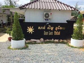 The exterior of Sun Leo Hotel with a black sign featuring a sun and text in a local language, a tiled roof, and potted plants. - Sun Leo Hotel (Sihanoukville)