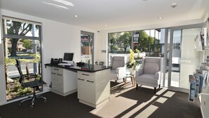 A modern office space with a desk, office chair, and a view of a street through large windows. - Bealey Plaza Motel (Christchurch)