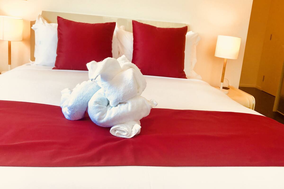 A neatly made bed with red and white bedding, two red pillows, and a white towel arranged in the center.