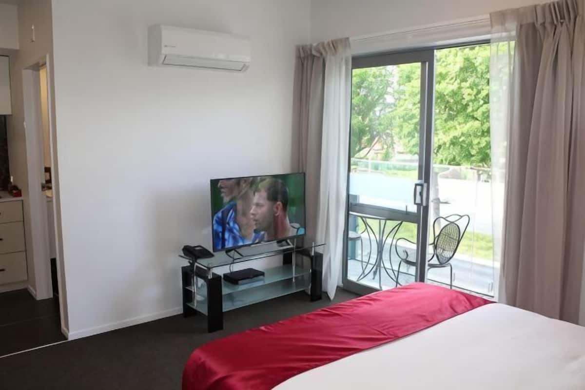 A hotel room with a bed, a television, a balcony with a chair, and a sliding glass door.
