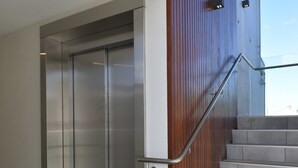 A modern elevator with a metallic finish, adjacent to a staircase with wooden paneling and a metal handrail. - Bealey Plaza Motel (Christchurch)