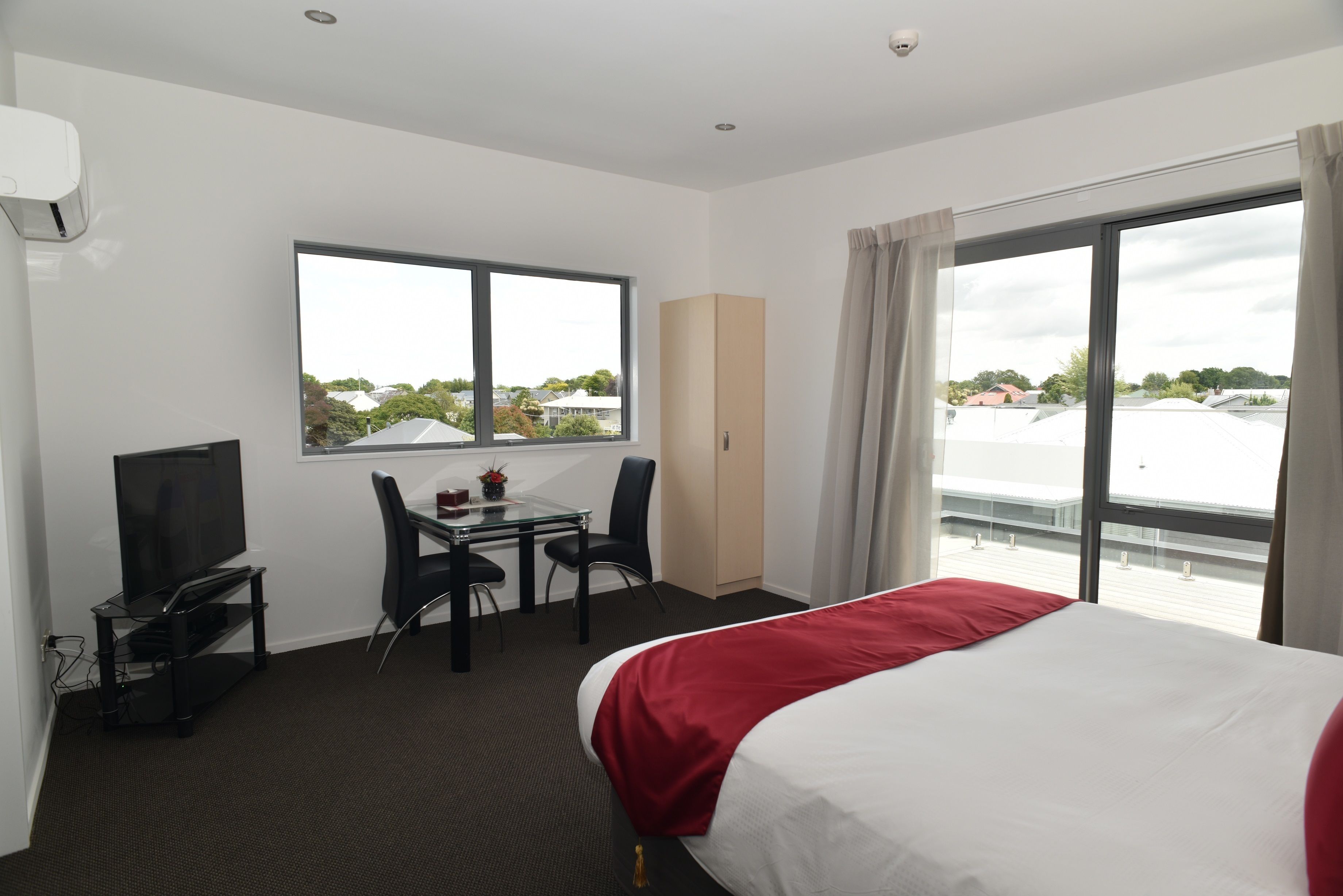 Une chambre d’hôtel comprenant un lit, une télévision, un bureau avec des chaises, une fenêtre et une vue sur l’extérieur.