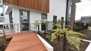 A modern building with a wooden deck, a wheelchair-accessible entrance, and a garden with ferns. - Bealey Plaza Motel (Christchurch)