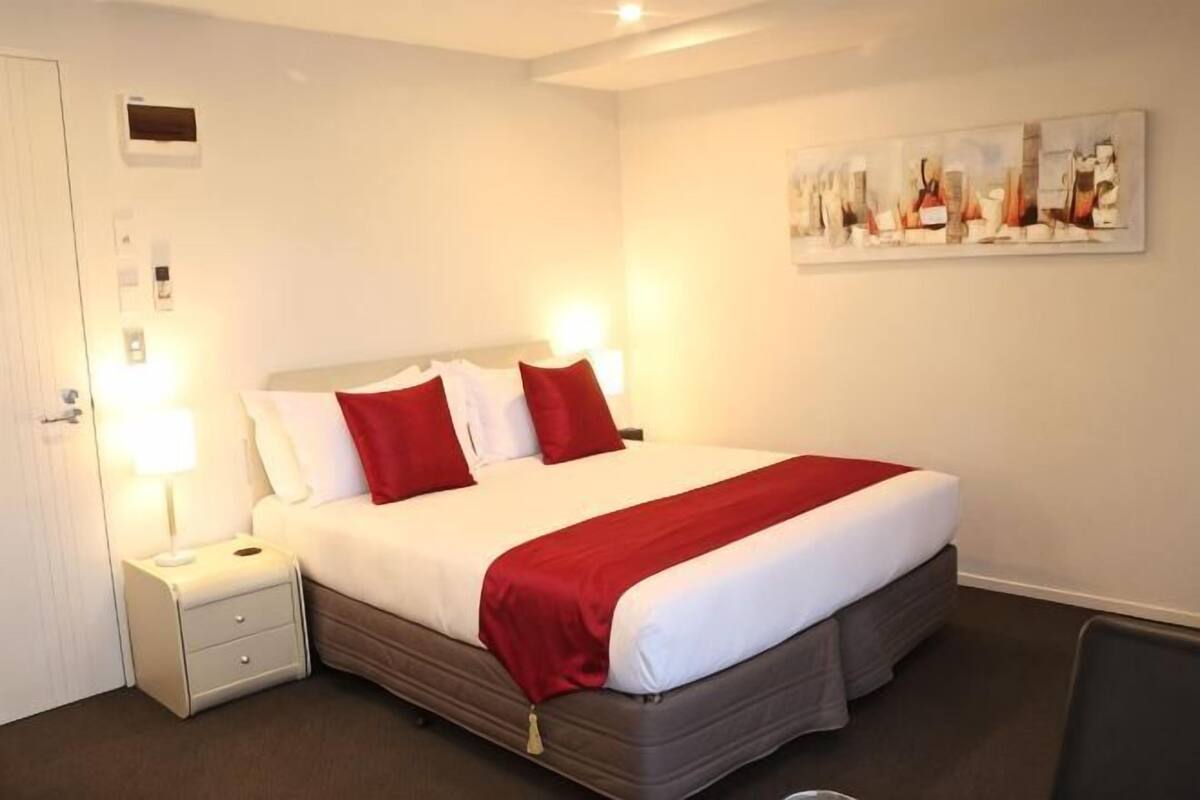 A hotel room with a bed, bedside lamps, a nightstand, a chair, and a painting on the wall.