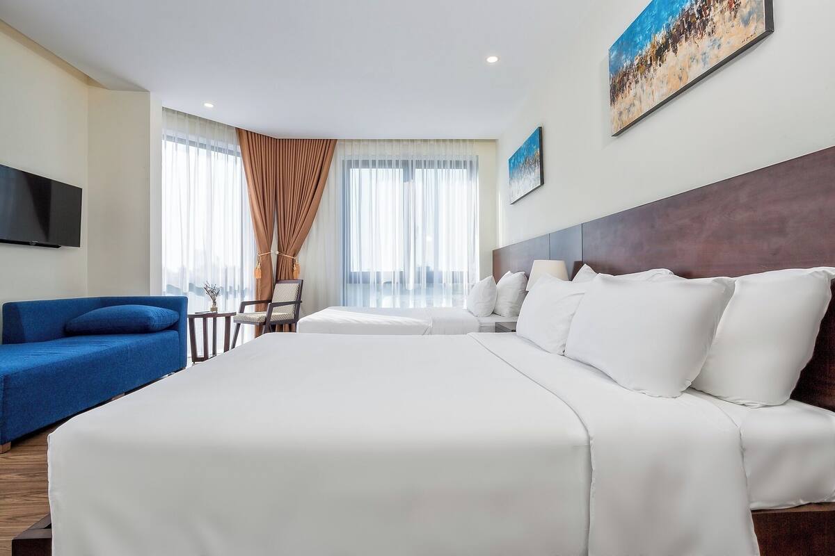 A hotel room with a large bed, a blue sofa, a chair, and a TV on the wall.