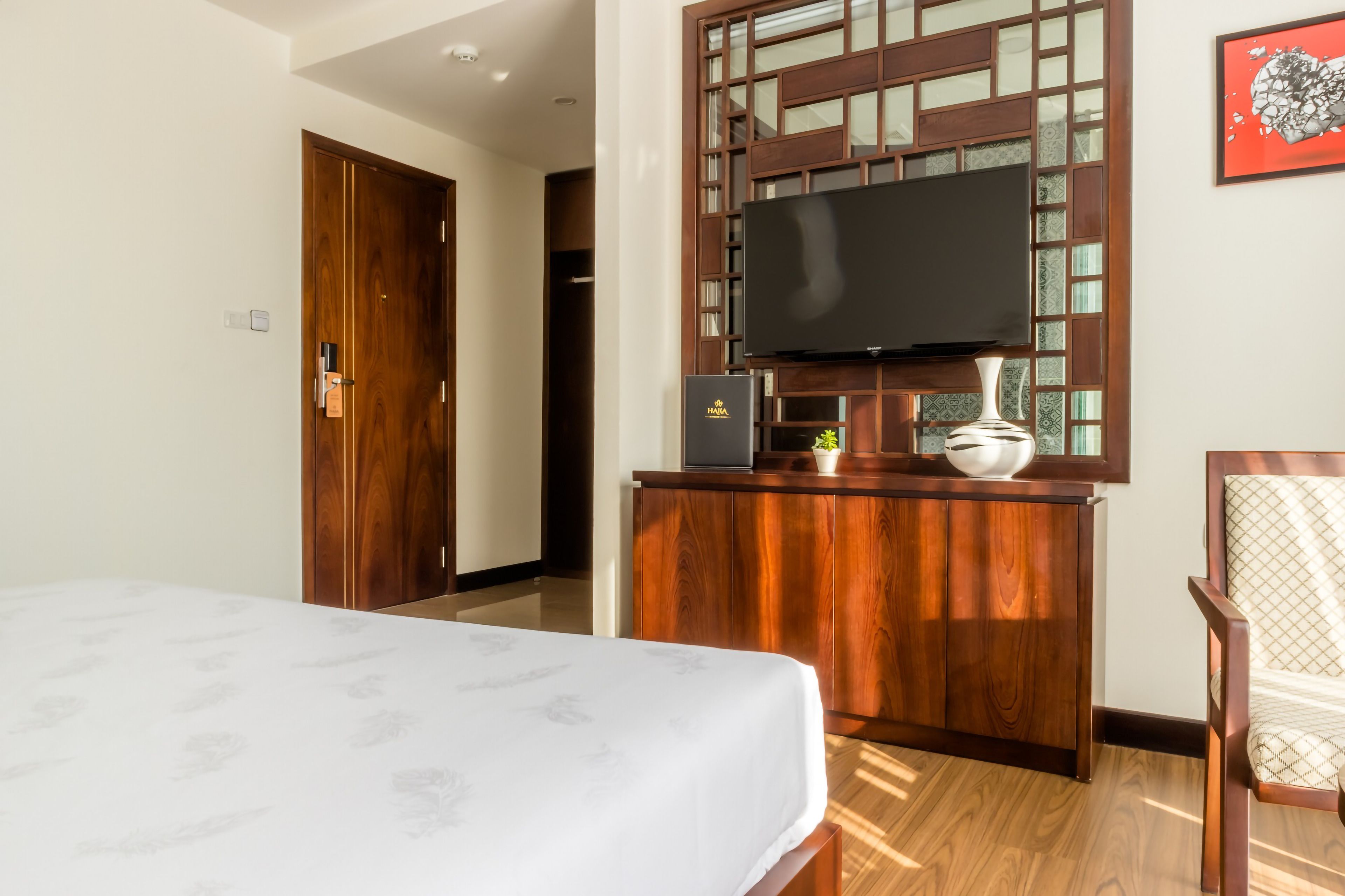 A hotel room with a bed, a wooden desk with a television, and a chair.
