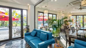 A modern hotel lobby with a blue sofa, dining area, and large windows with a view of the street. - Haka Hotel & Apartment (Da Nang)
