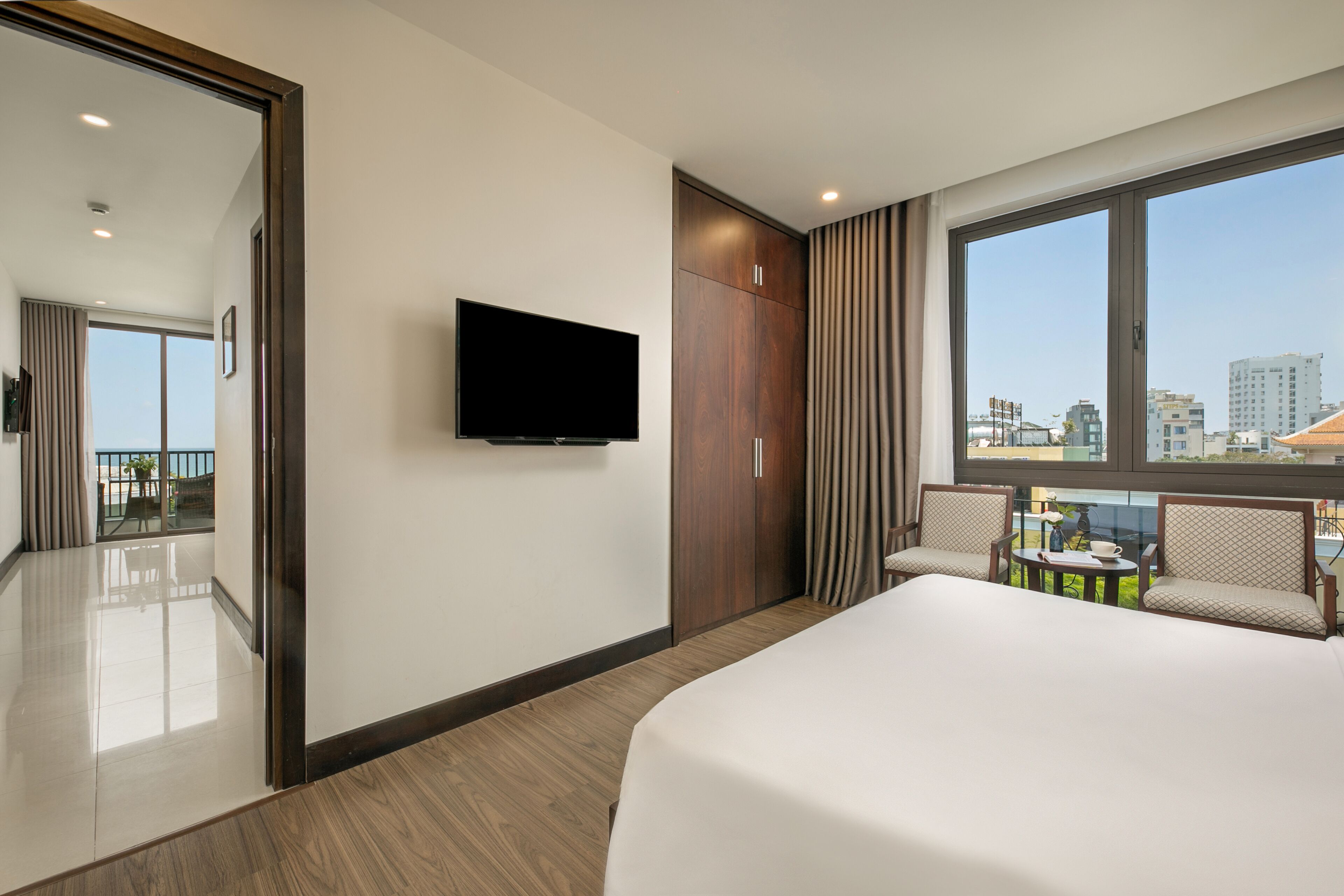 Une chambre d’hôtel avec un grand lit, un téléviseur fixé au mur, une armoire et un balcon offrant une vue sur la ville.