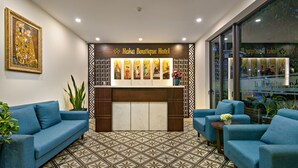 A reception area with a wooden reception desk, blue sofas, patterned floor tiles, and a framed artwork on the wall. - Haka Hotel & Apartment (Da Nang)