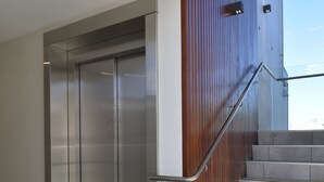 A modern elevator with a metallic finish, adjacent to a staircase with wooden paneling and metal handrails. - 103 Prince of Bealey Motel (Christchurch)