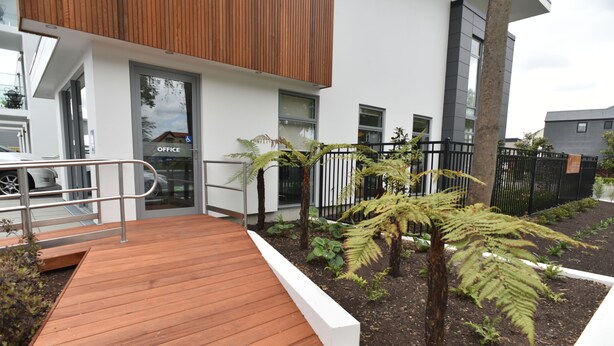 A modern building with a wooden deck, a wheelchair-accessible entrance, and a garden with ferns. - 103 Prince of Bealey Motel (Christchurch)