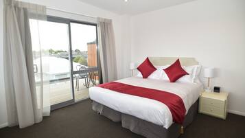 A hotel room with a large bed, a nightstand, a lamp, and a view of the outside through a sliding door.