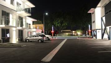 Un edificio moderno con un estacionamiento, una calle con coches y un árbol al fondo.