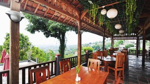 Un área de comedor al aire libre con mesas y sillas de madera, rodeada por una pérgola de madera con plantas colgantes.
