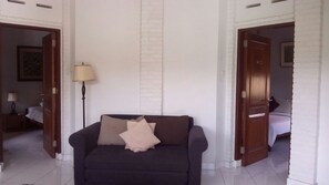 A room with a dark-colored sofa, a lamp, and a white brick wall. There are doors leading to other rooms.