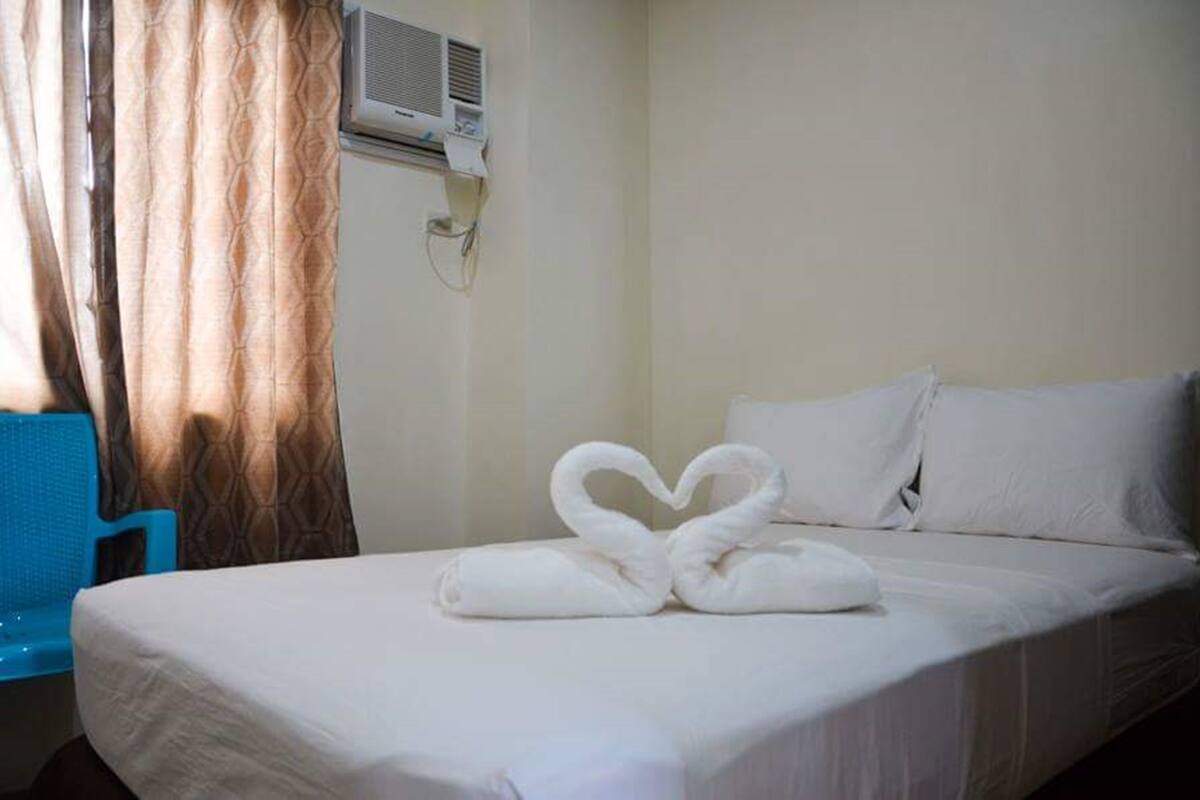 Una habitación de hotel con una cama, una silla azul y un equipo de aire acondicionado en la pared.