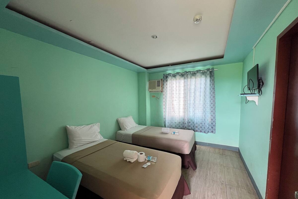 Habitación de hotel con dos camas, una mesita, un televisor y una ventana con cortinas.