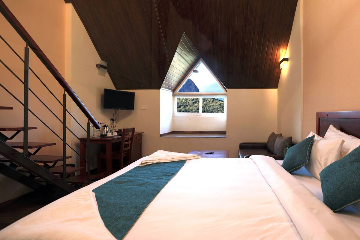 Ein Schlafzimmer mit Bett, Schreibtisch, Stuhl, Fenster mit Aussicht und einer Treppe.