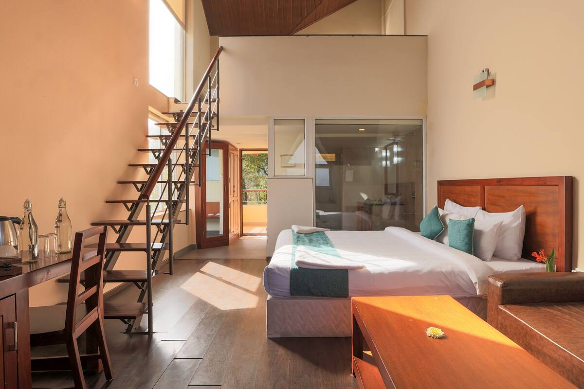 Ein modernes Hotelzimmer mit einer Holztreppe, einem Bett mit Kissen, einem Holztisch und Blick ins Freie.