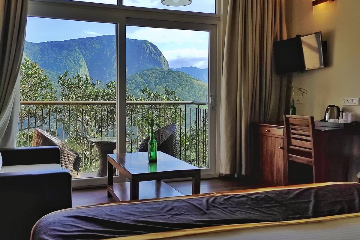 Ein Hotelzimmer mit Balkon, einem Bett, einem Tisch, einem Stuhl und einem Schreibtisch mit Flachbildfernseher.