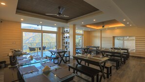 Un vaste espace dédié à la salle à manger, avec de nombreuses tables et des bancs, de grandes fenêtres offrant une vue sur les montagnes et des ventilateurs de plafond.