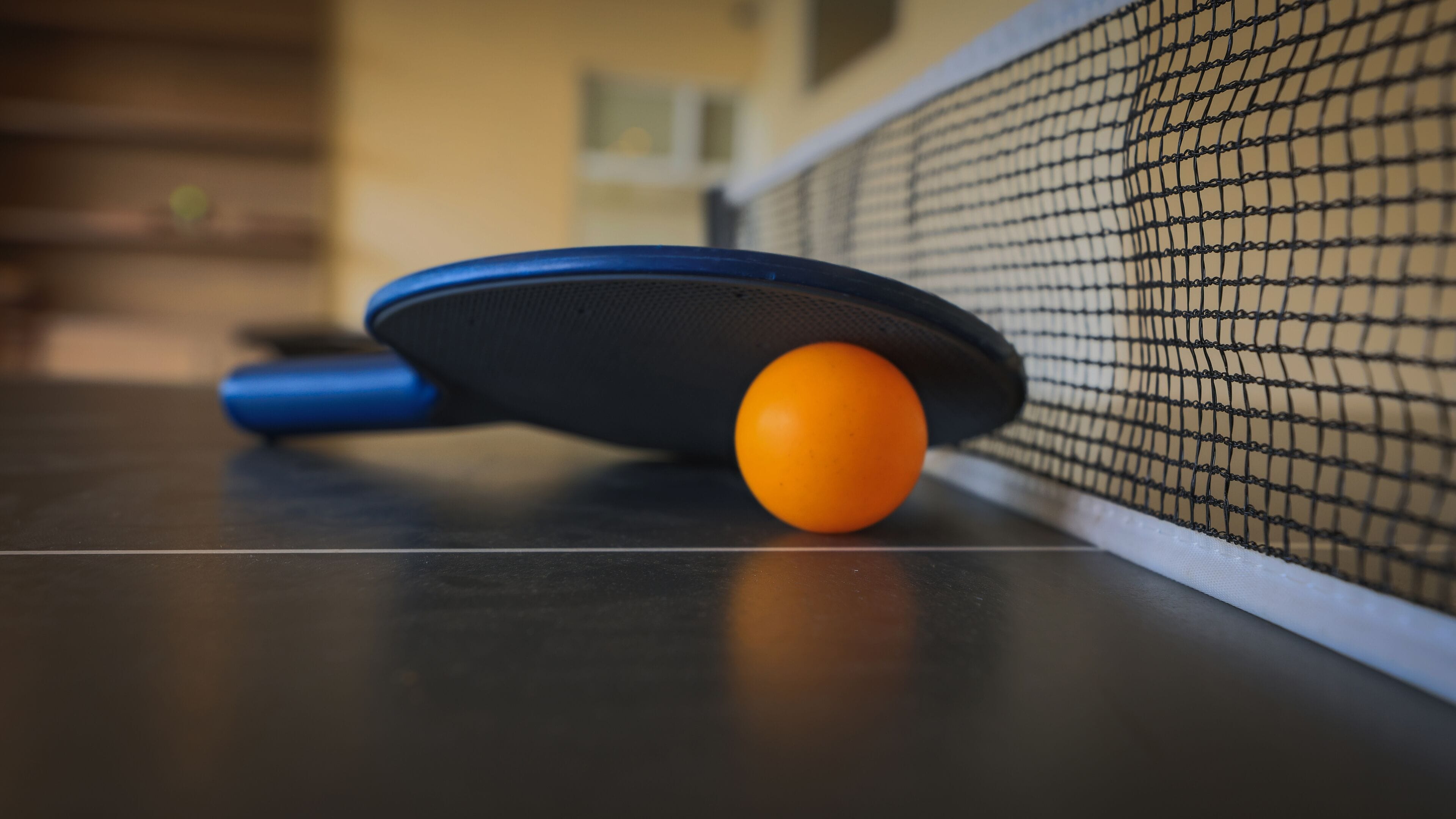 Una mesa de tenis de mesa con una paleta azul y una pelota naranja.