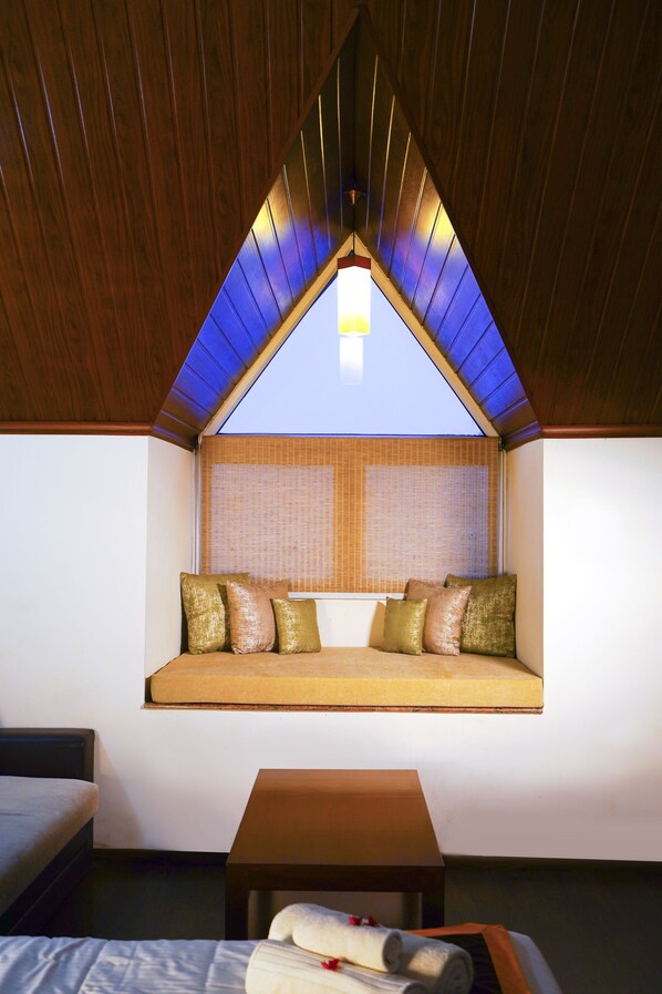 A cozy room with a sloped ceiling, a built-in bench with cushions, a small table, and a window with blinds.