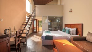 Une chambre d’hôtel moderne avec un escalier en bois, un grand lit avec de nombreux oreillers, une table en bois et une vue sur le balcon extérieur.