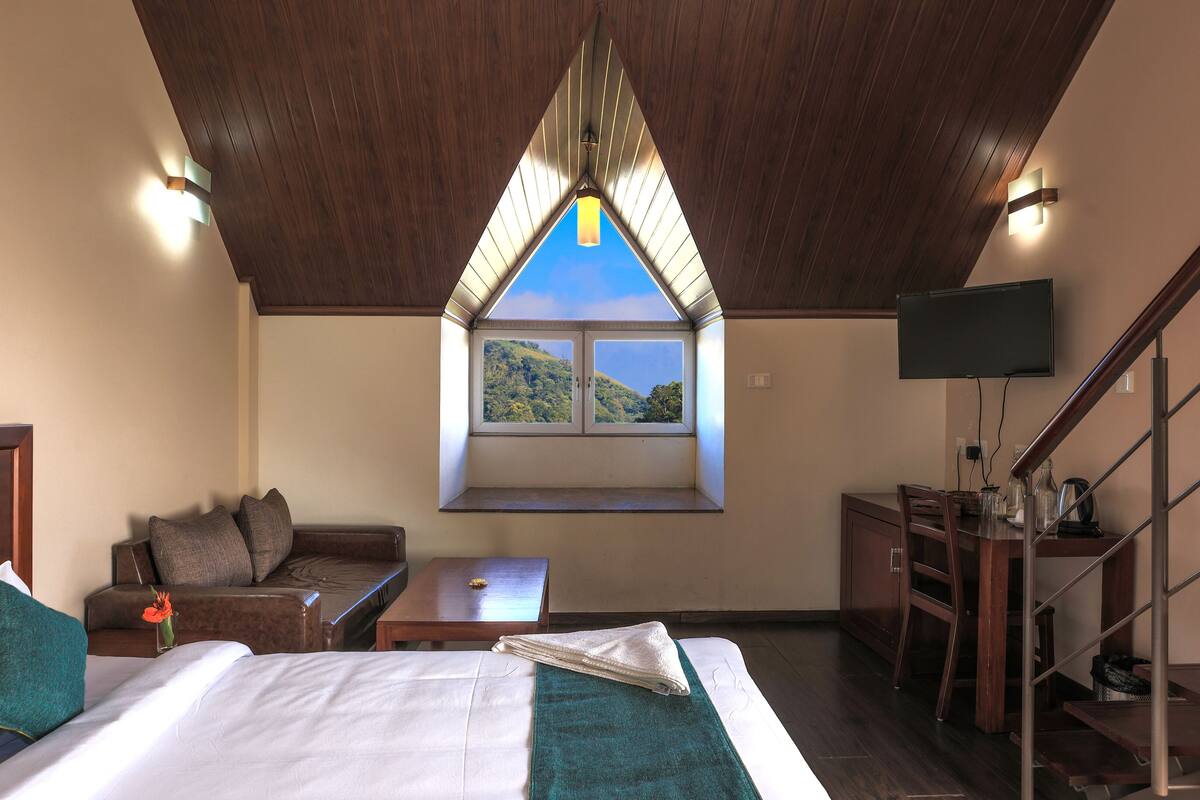 Ein Schlafzimmer mit einem großen Bett, einem Fenster mit Bergblick, einem an der Wand befestigten Fernseher und einer Holzbalkendecke.