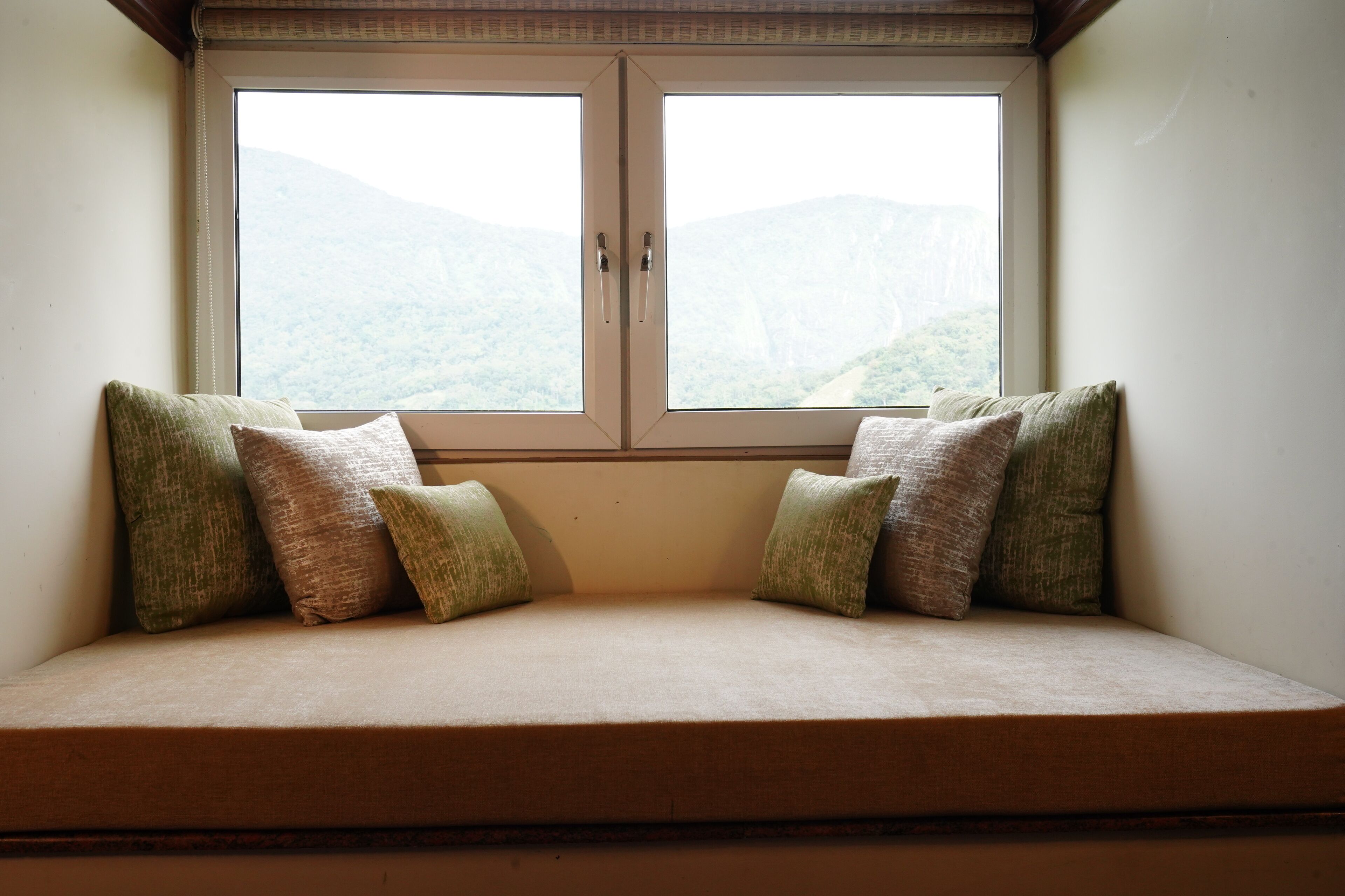Sitzplatz am Fenster mit Kissen, Blick auf Berge und ein Holzbalken darüber.