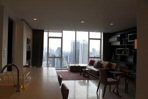 A modern living room with a city view, a dining area, and a bookshelf.