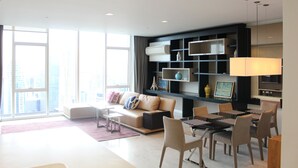Een moderne woonkamer met een bank, salontafel, eettafel en stoelen. Er is een groot raam met uitzicht op de stad.