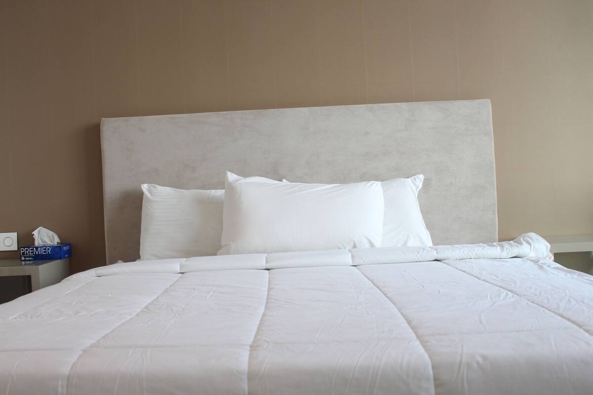 Een keurig opgemaakt bed met een groot hoofdeinde, witte beddengoed en een zakdoekendoos op het nachtkastje.