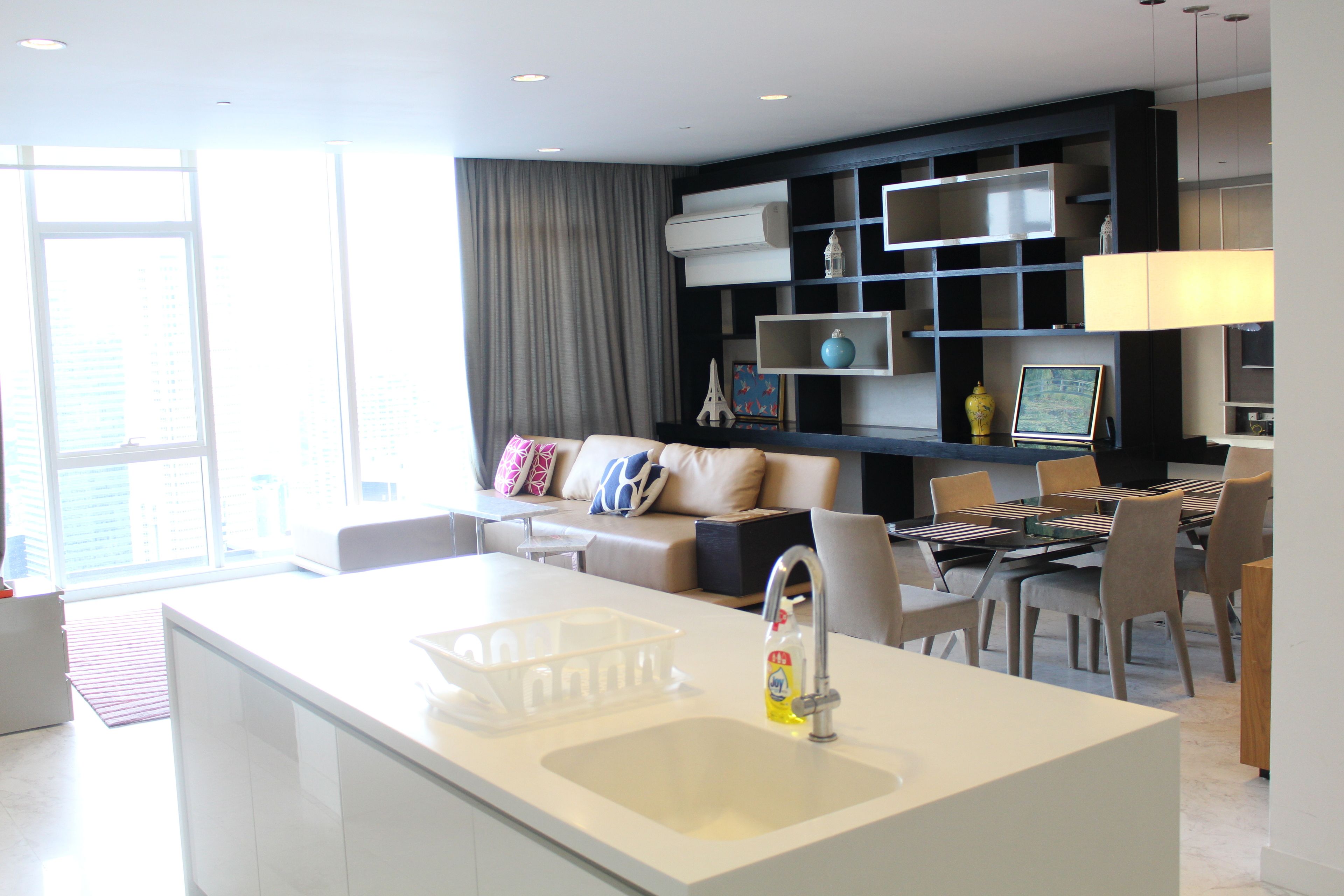 A modern living room with a kitchen area, a dining table, and a sofa with cushions.