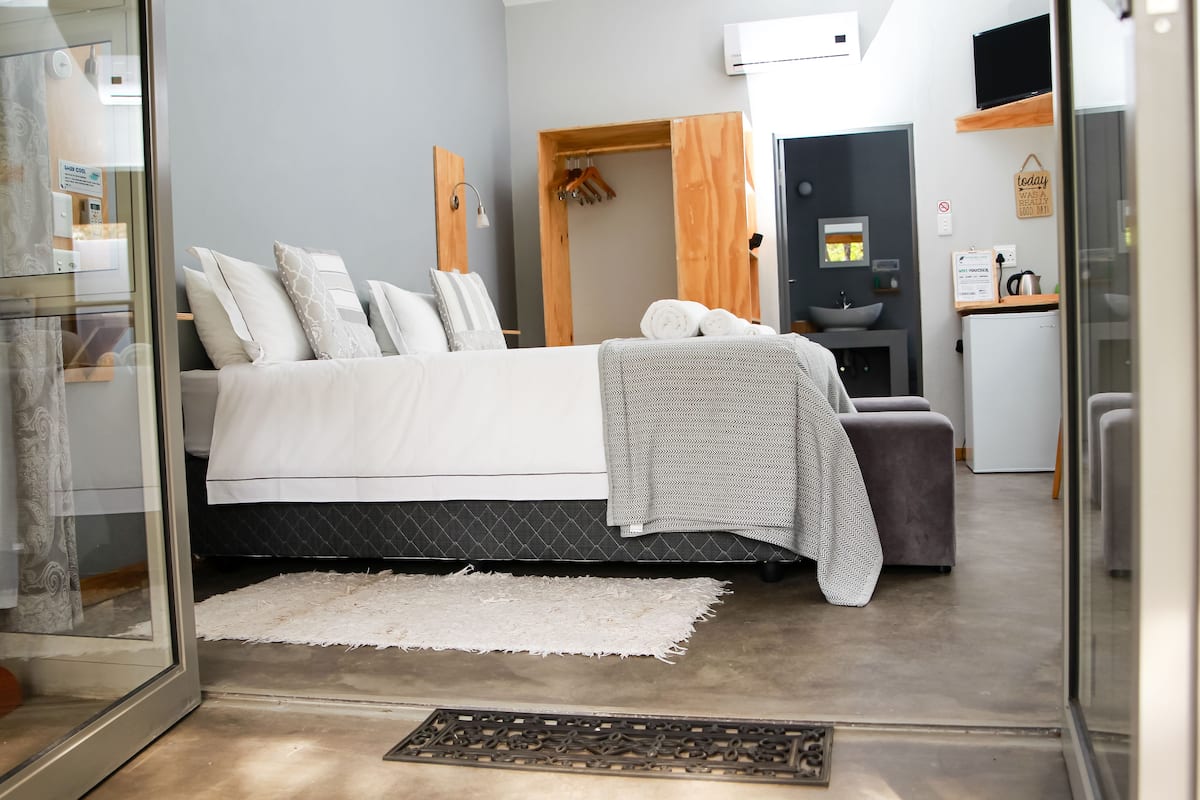 Un dormitorio moderno con cama, mesita de noche y un pequeño rincón de descanso.