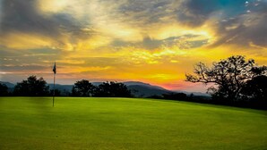 Un terrain de golf avec un mât de drapeau, des arbres et un coucher de soleil en arrière-plan.
