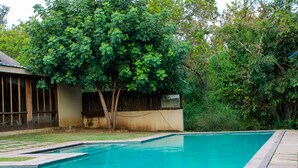 Une piscine rectangulaire, bordée d’une terrasse carrelée, entourée d’une pelouse et d’arbres.
