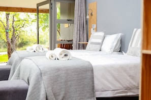 A hotel room with two beds, a wooden ceiling, a window with a view of trees, and a small table with a lamp. - Bushbaby Lodge at Nkonyeni (Sidvokodvo)