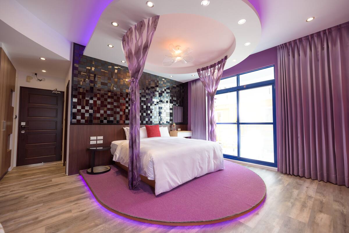 A modern bedroom with a large bed, purple curtains, and a checkered wall.