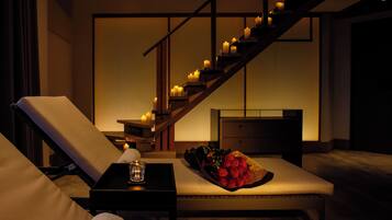 A modern room with a staircase, a lounge chair, a bedside table with a glass, and a bouquet of red roses.