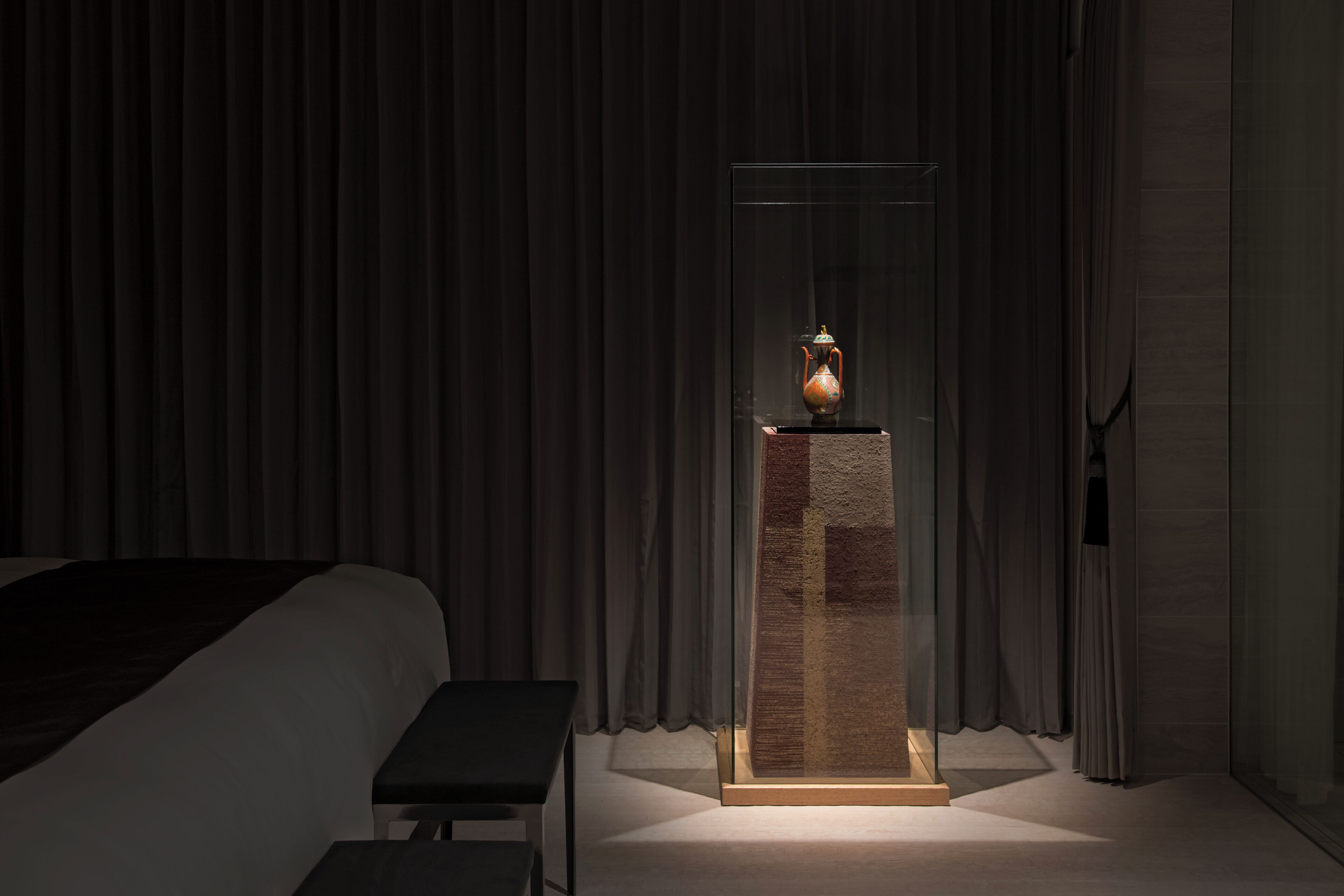 A modern hotel room with a bed, a small table, and a decorative vase on a stand.