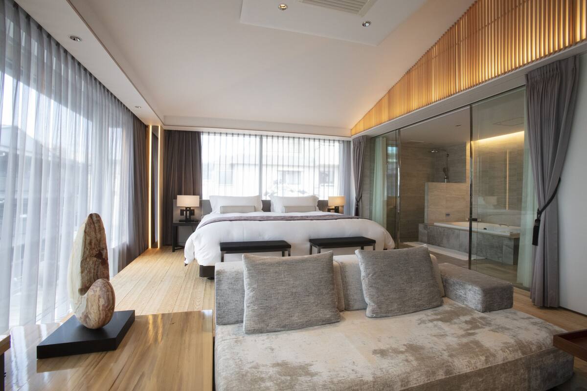 Ein modernes Hotelzimmer mit einem großen Bett, einer Sitzecke, einer Duschkabine aus Glas und Blick auf die Stadt.