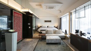 A modern hotel room with a large bed, a sitting area with a sofa and ottoman, a small kitchen area, and large windows offering a view. - Art Mon Zen Kyoto (Kyoto)