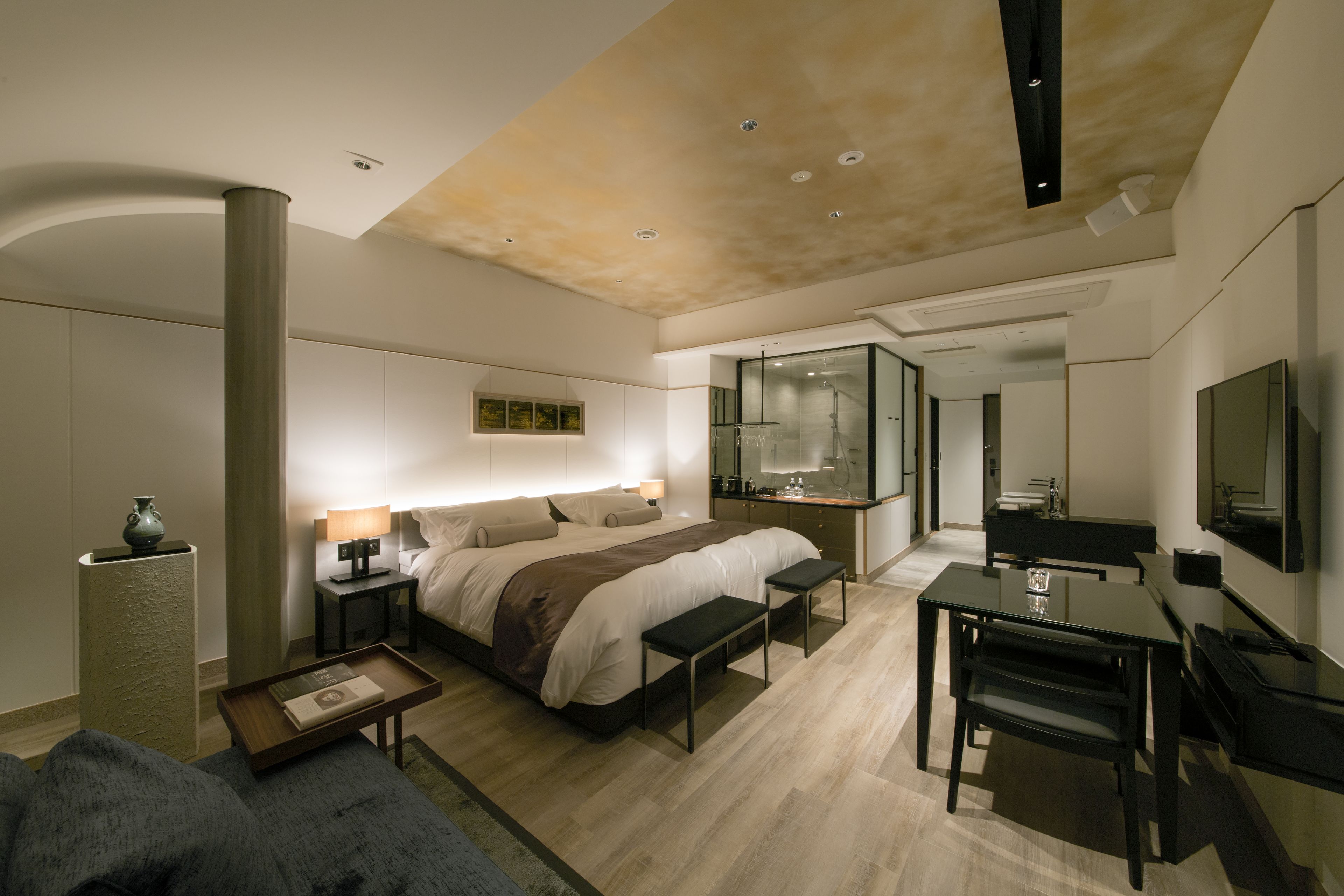 A modern hotel room with a large bed, bedside tables, a desk, and a mirror.