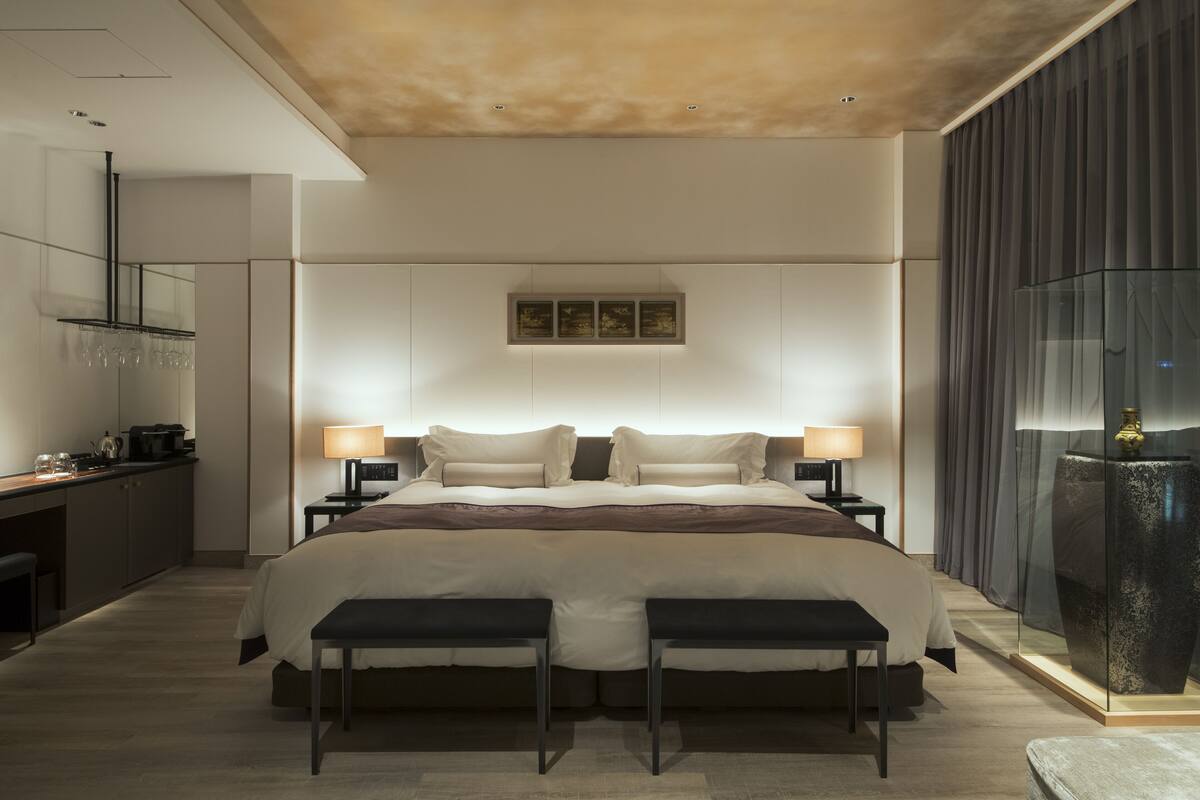 Ein modernes Hotelzimmer mit einem großen Bett, Nachttischen, einem Schreibtisch und einer Glastrennwand.
